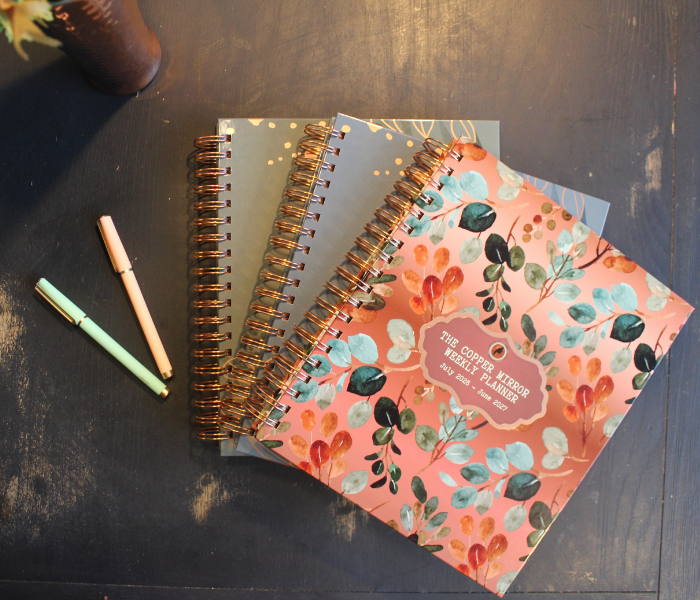 The Copper Mirror Weekly Planner — all three cover colors fanned out on a table